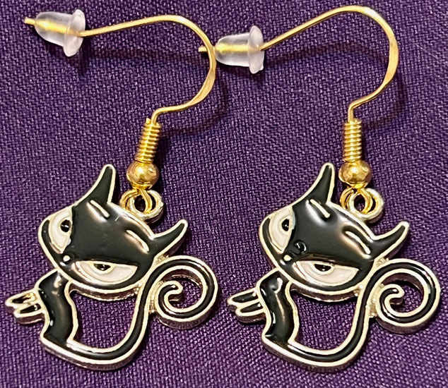 Photo of a pair of earings of enameled black cats with large heads and eyes and thin little bodies and a long curled tail.